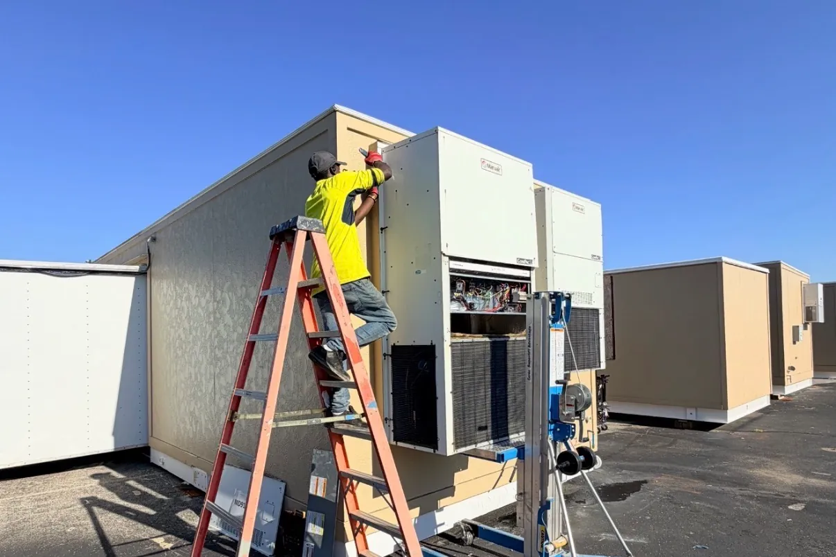 Prime Guard technician servicing wall-mount HVAC units on a modular building.